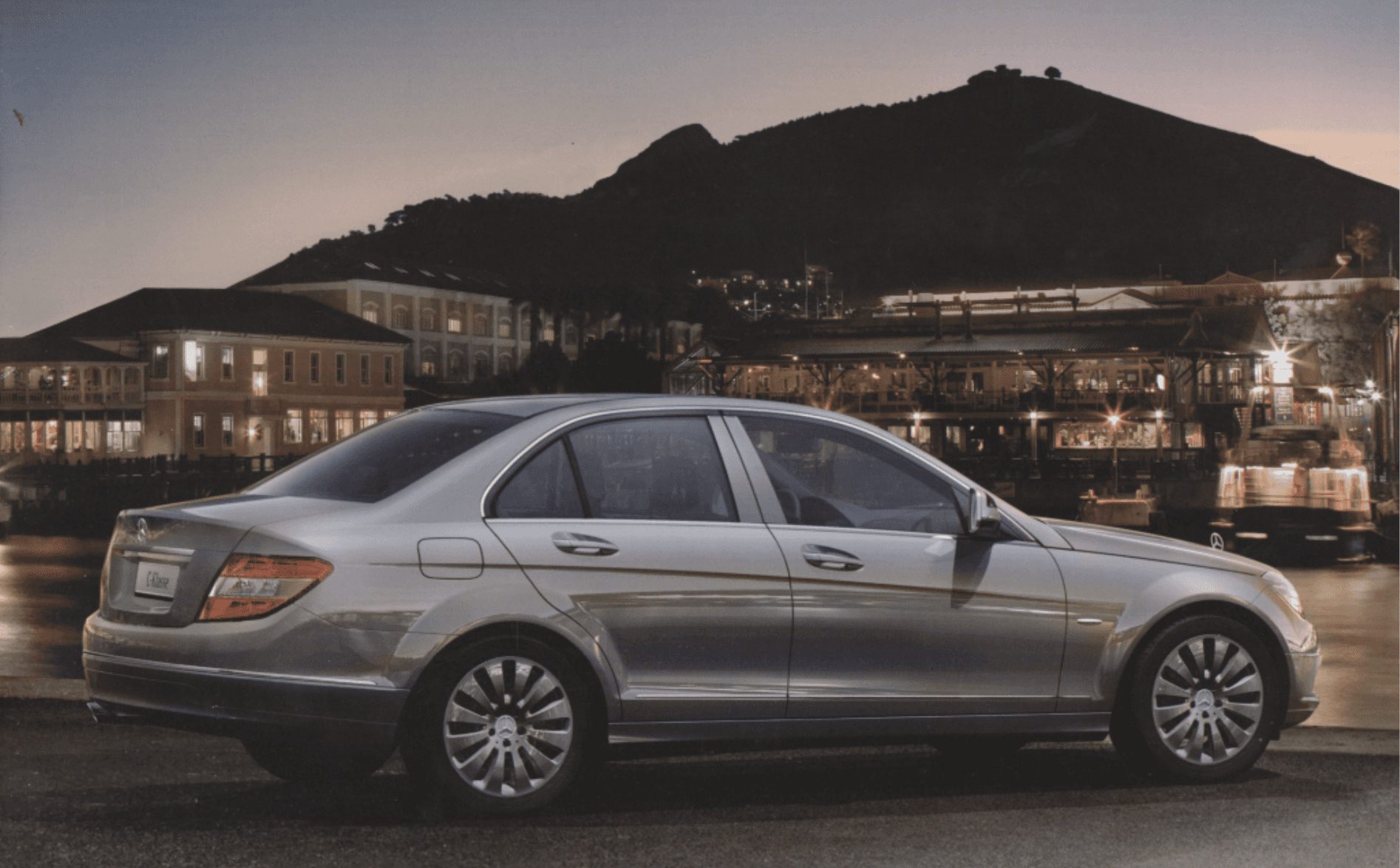 Silver sedan parked at night with city lights in background