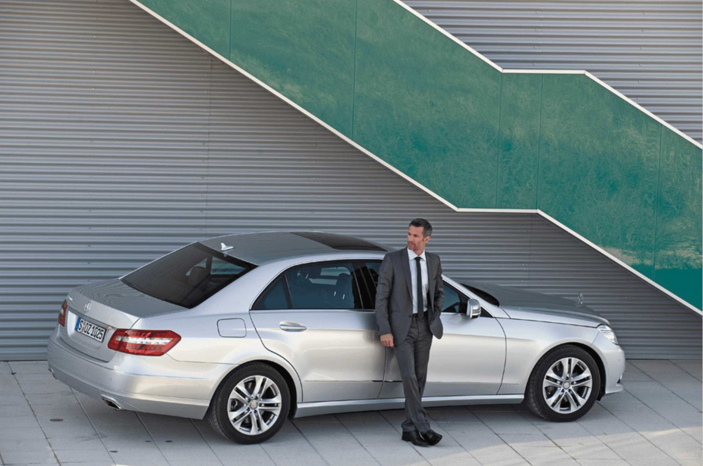 Rear angle view with a man in a suit leaning against the car
