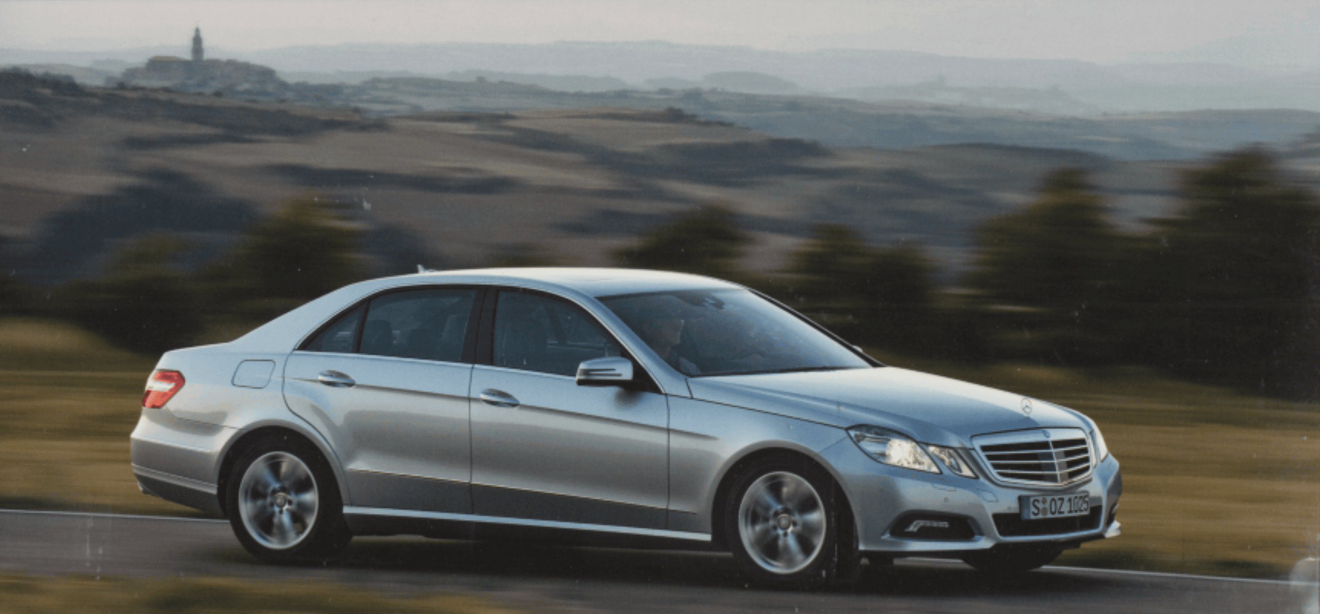 Side profile of the car driving through a landscape with rolling hills